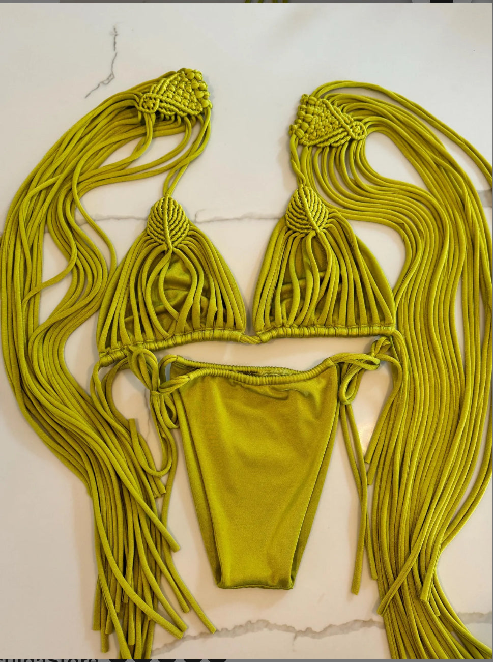 Green macrame bikini set on a white marble surface